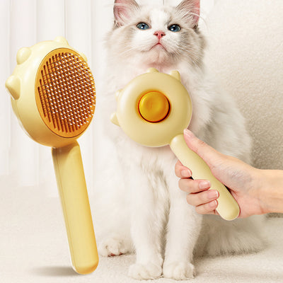 Cat being groomed with a yellow grooming brush held by a hand, with a white background